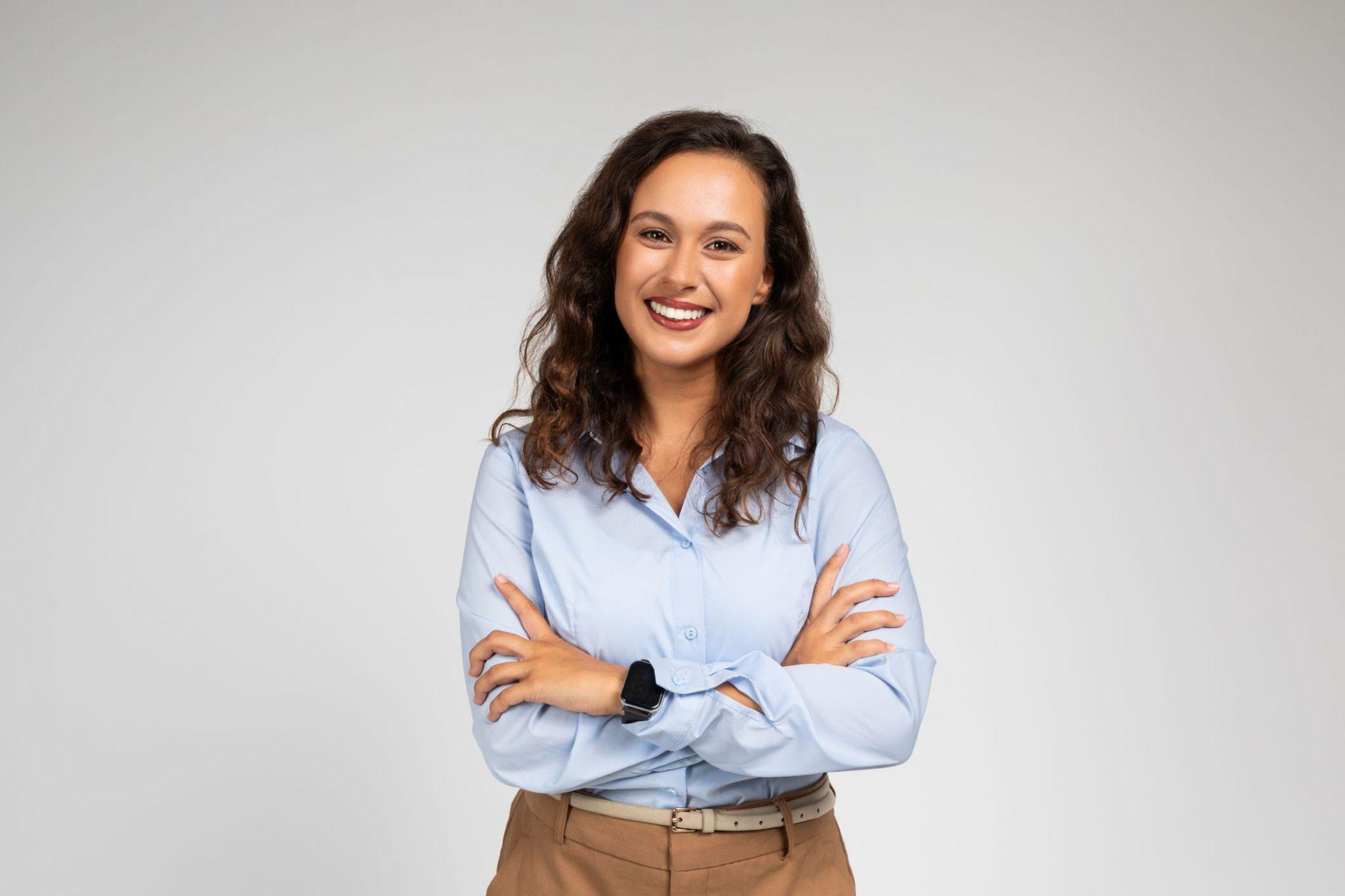 Smiling person in blue shirt with crossed arms against a plain background.