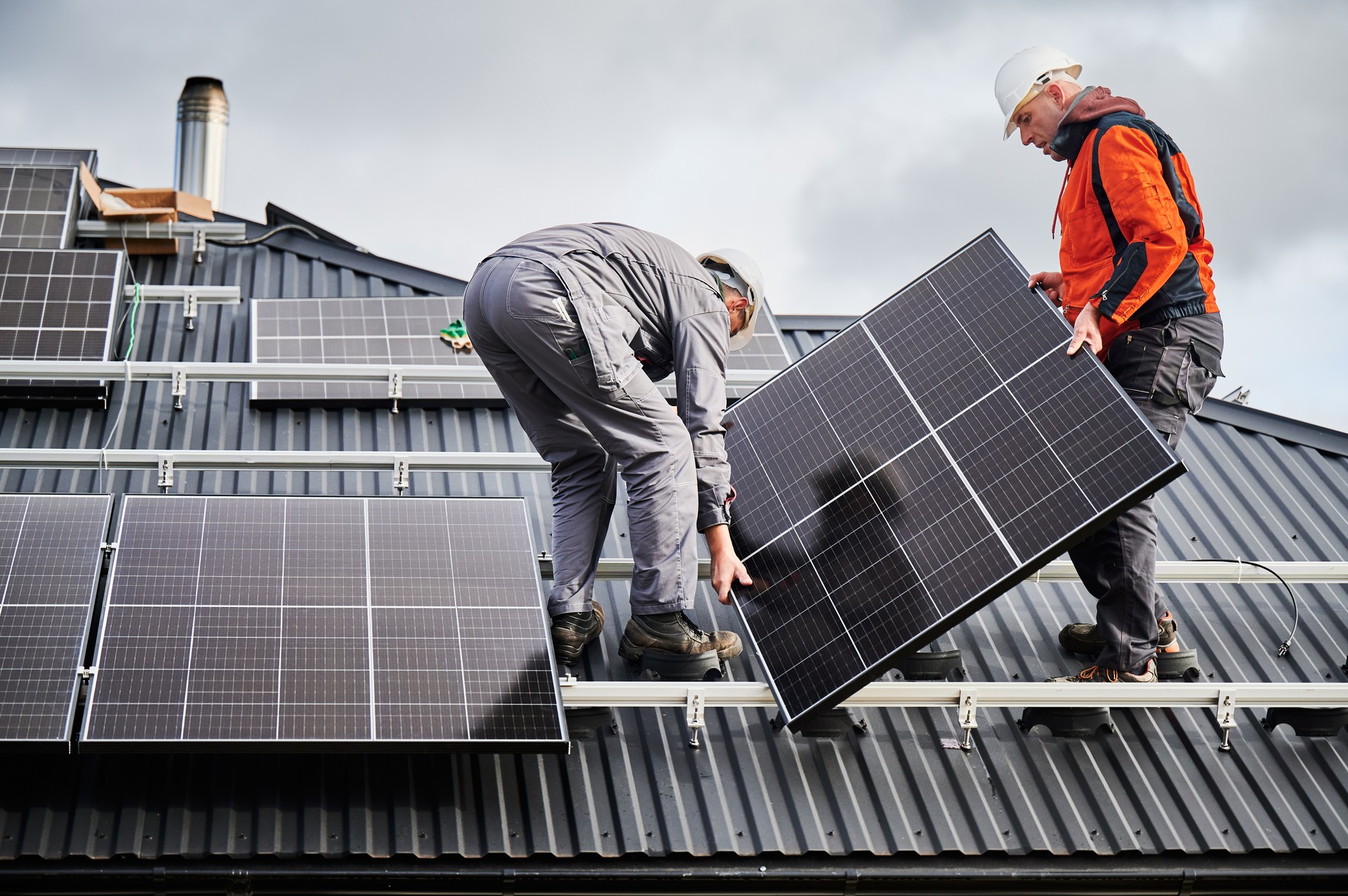 Techniker, die ein Photovoltaik-Solarmodul tragen, während sie eine Solaranlage auf dem Dach des Hauses installieren