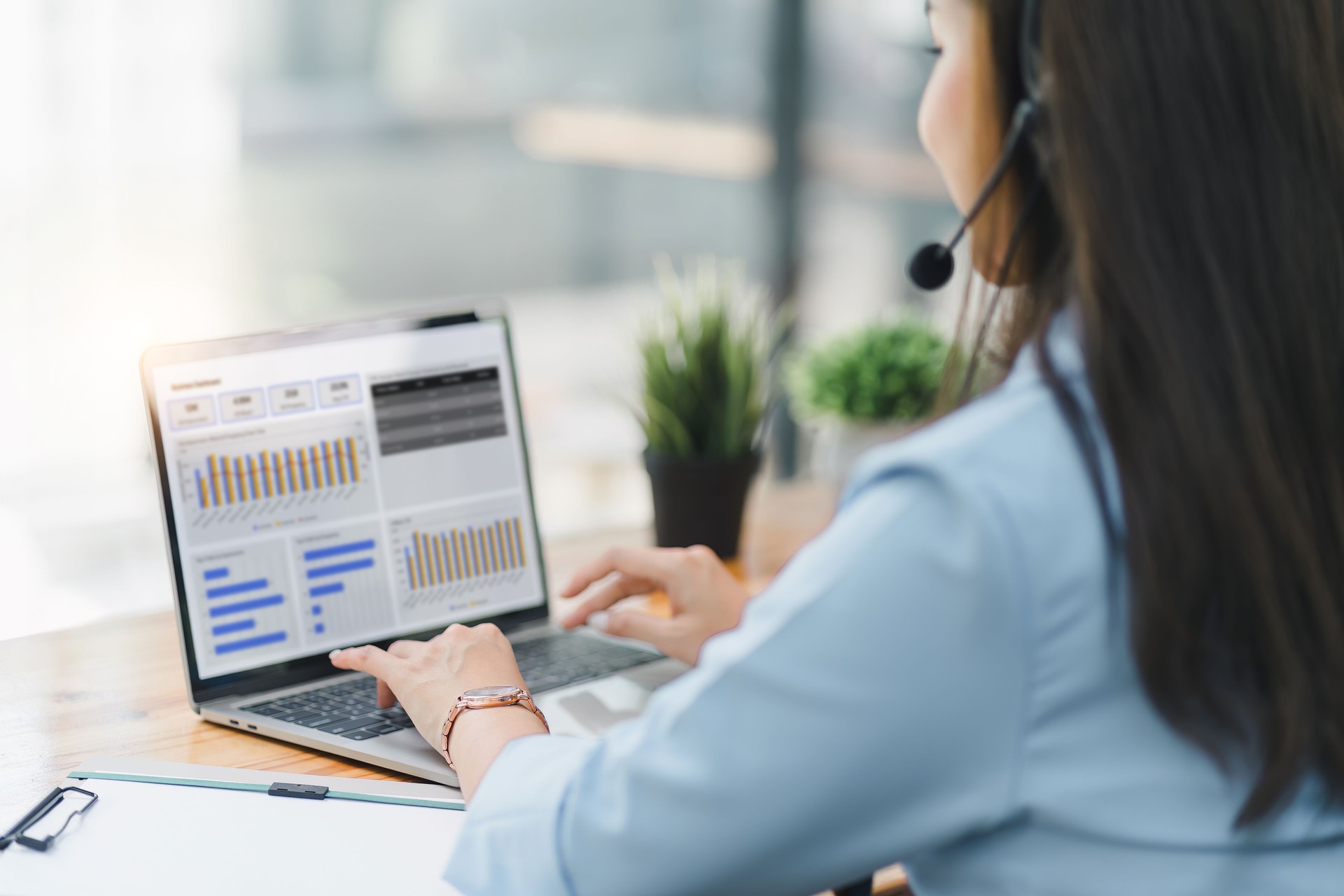 Operator wearing a headset, using a dashboard on laptop for data analysis in modern office. Selective focus