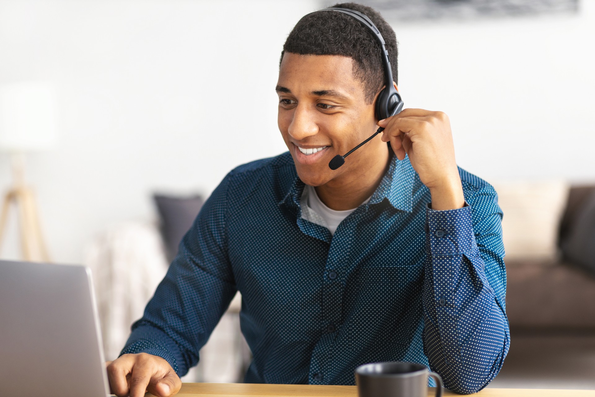 Afroamerikaner junger Mann Kundensupport Call-Center-Operator oder Rezeptionist, der am Arbeitsplatz in einem modernen Büro sitzt und einen Kunden berät, ein Headset benutzt, lächelt freundlich